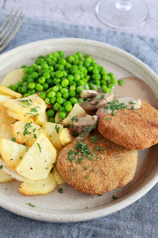 Filetes rusos acompañados de salsa de champiñones, guisantes y patatas asadas