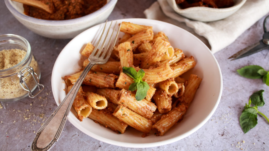 Plato de pasta tortiglioni con pesto rosso y decorada con albahaca fresca