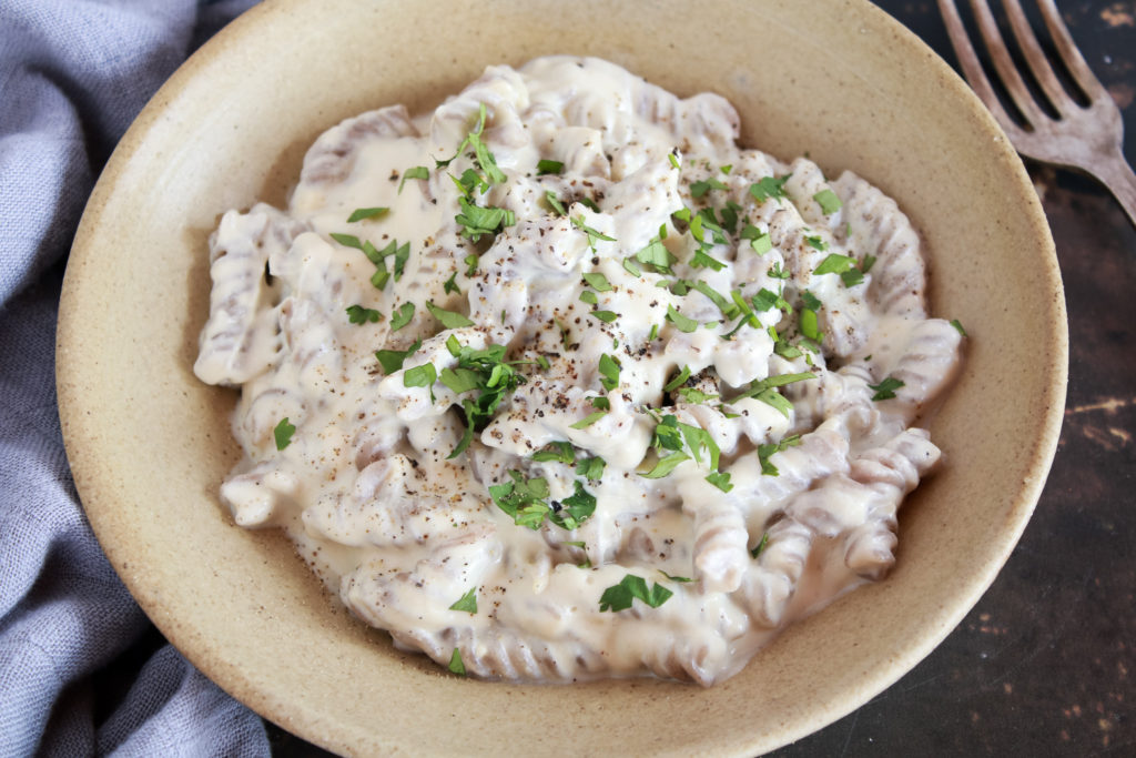 Plato de pasta fussilli con salsa Alfredo, blanca y decorada con perejil fresco picado