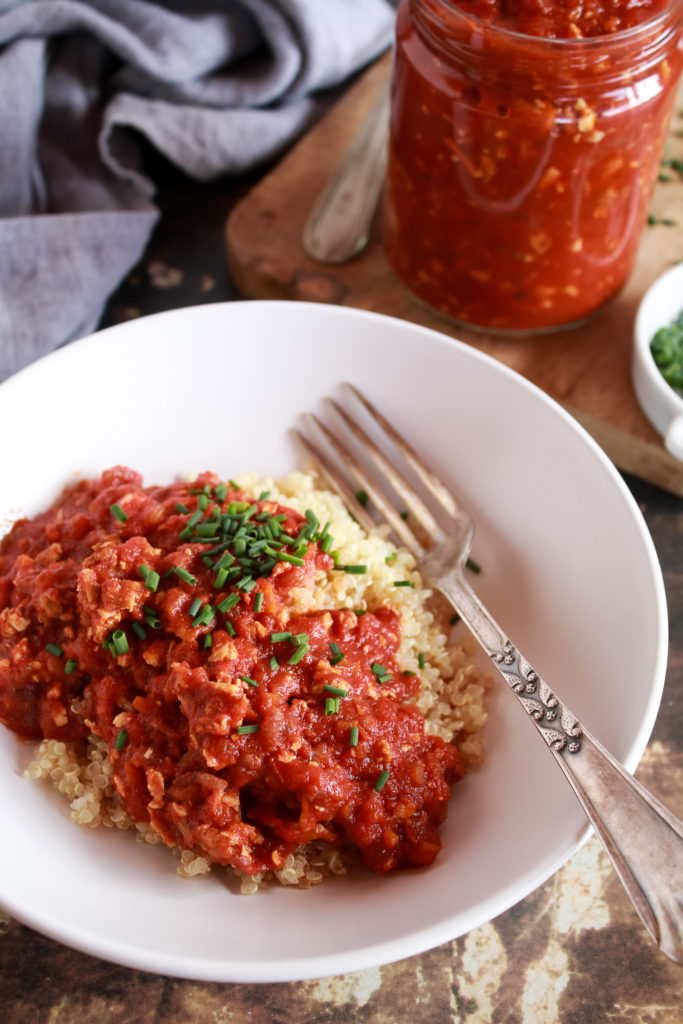 Plato de quinoa con boloñesa de tofu y un tenedor, aparece un bote de boloñesa de tofu de fondo