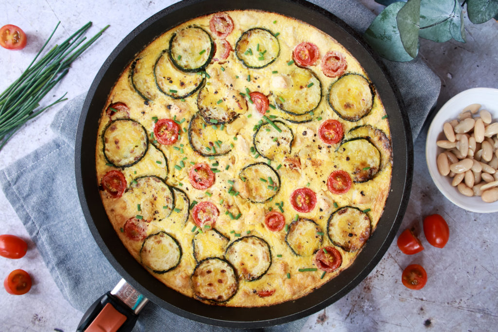 Frittata vegana en un sartén con tomates cherry y calabacín a la plancha en la superficie decorada con cebollino fresco y pimienta molida