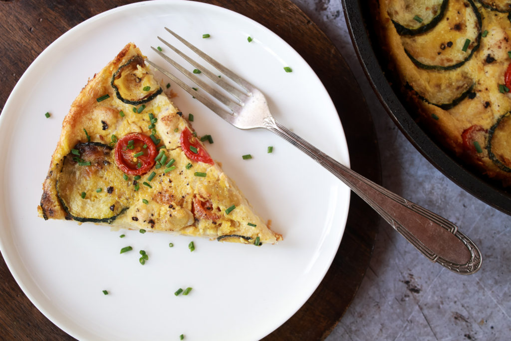 Porción de frittata vegana en un plato junto a un tenedor y la sartén con el resto de la elaboración al lado