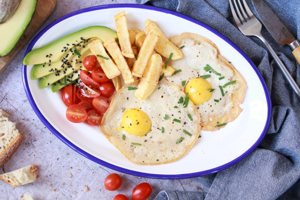 Dos huevos fritos veganos en una bandeja ovalada junto a patatas fritas, tomates cherry y aguacate