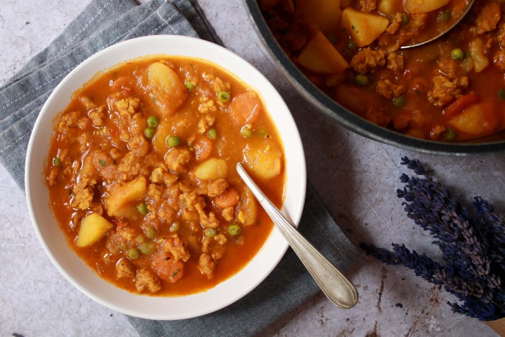 Plato de patatas guisadas con soja texturizada y verduras junto a la cacerola con el resto del guiso