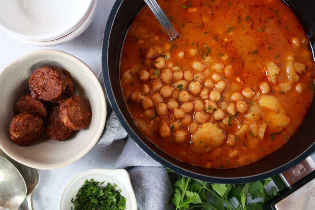 Guiso de garbanzos con chorizo vegano en una olla y unos chorizos fritos en un cuenco