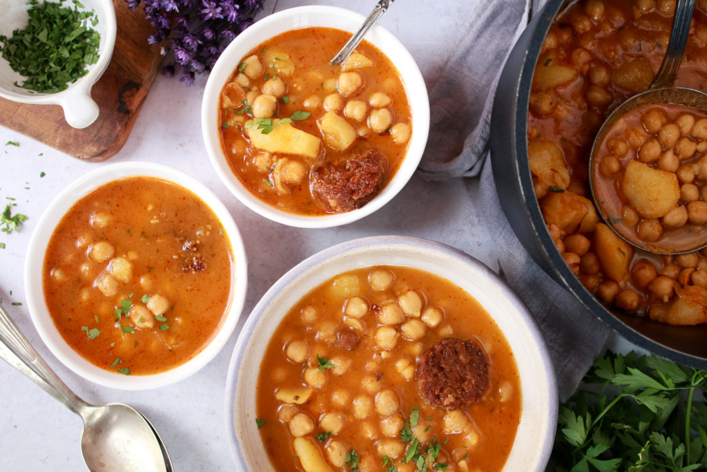 Guiso de garbanzos con chorizo vegano y tres cuencos servidos al lado de una cacerola.