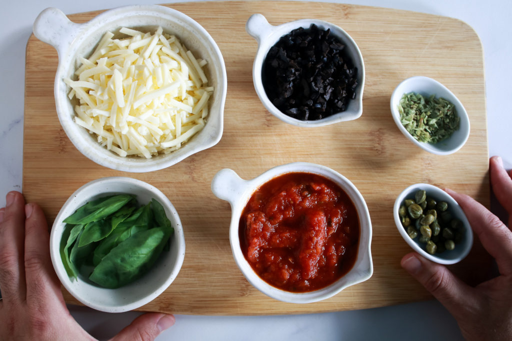 Ingredientes para la corona de hojaldre, salsa de tomate, queso vegano, aceitunas, albahaca, orégano y alcaparras